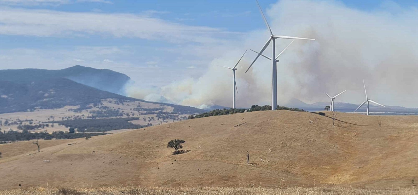 smoke from a hill behind wind turbines. 