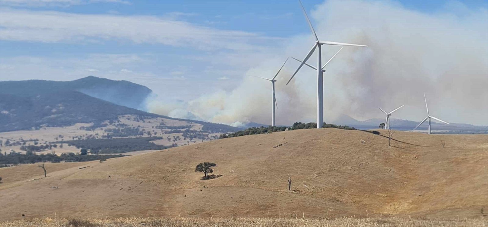smoke from a hill behind wind turbines. 