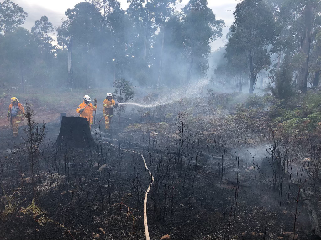 fire fighter on burnt out ground with a hose.